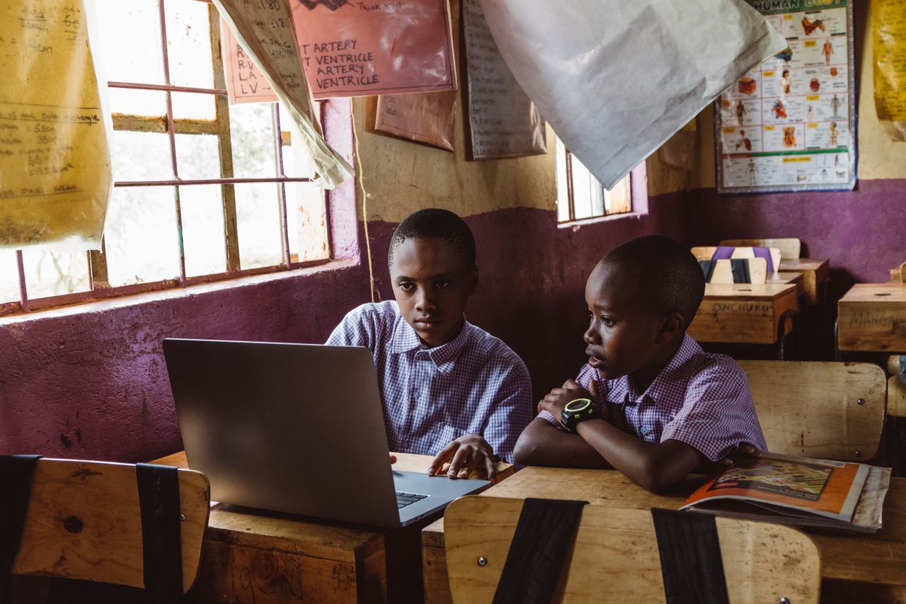 Two boys in a classroom using a laptop for studying, fostering learning and teamwork.